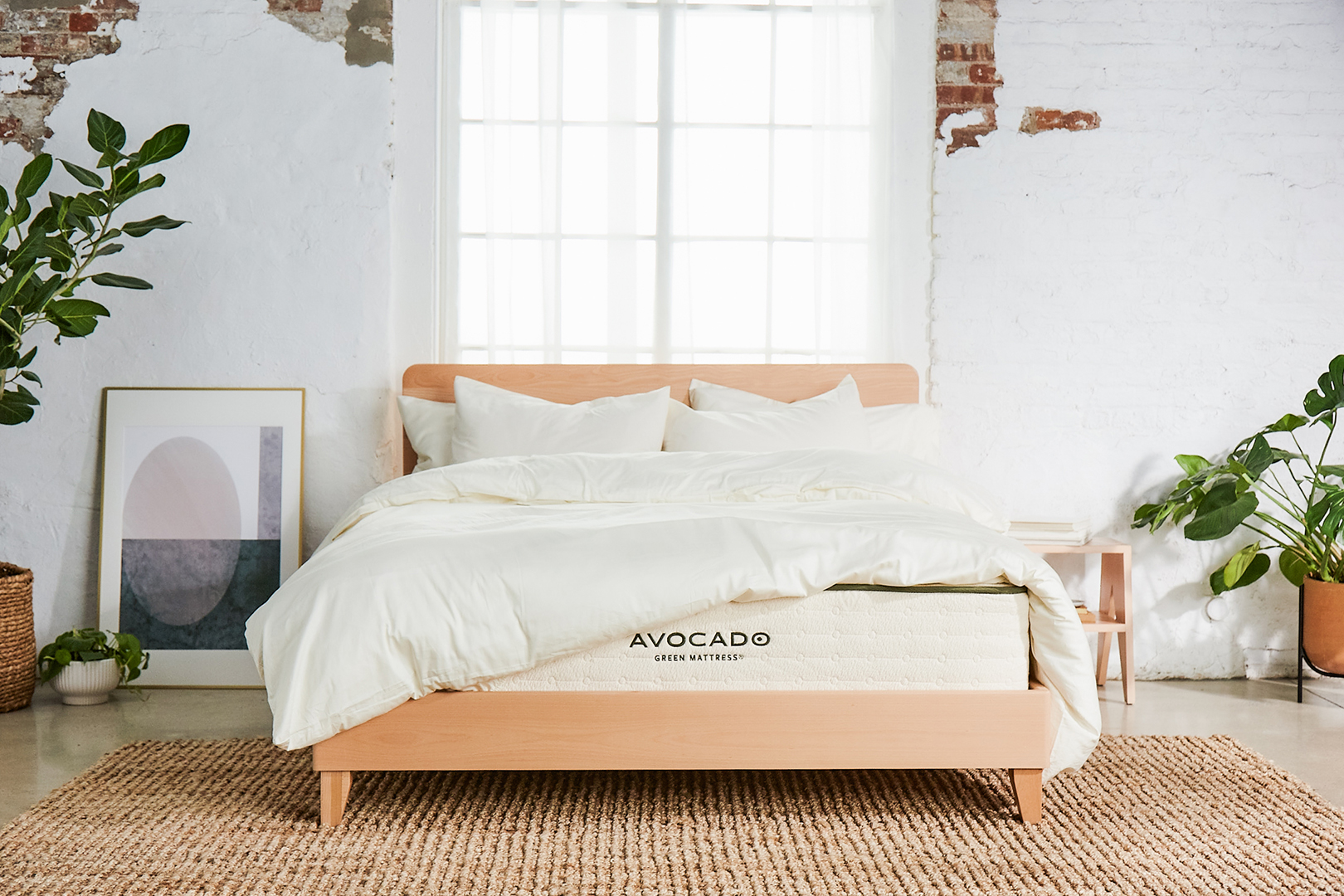 Wood bed frame with white bedding, jute rug, and plants on either side. 