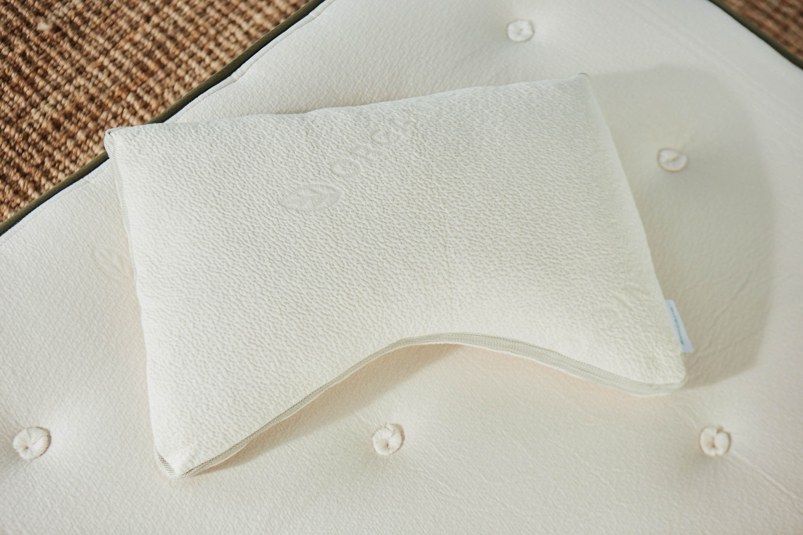 White cotton pillow on white mattress with jute rug in background.