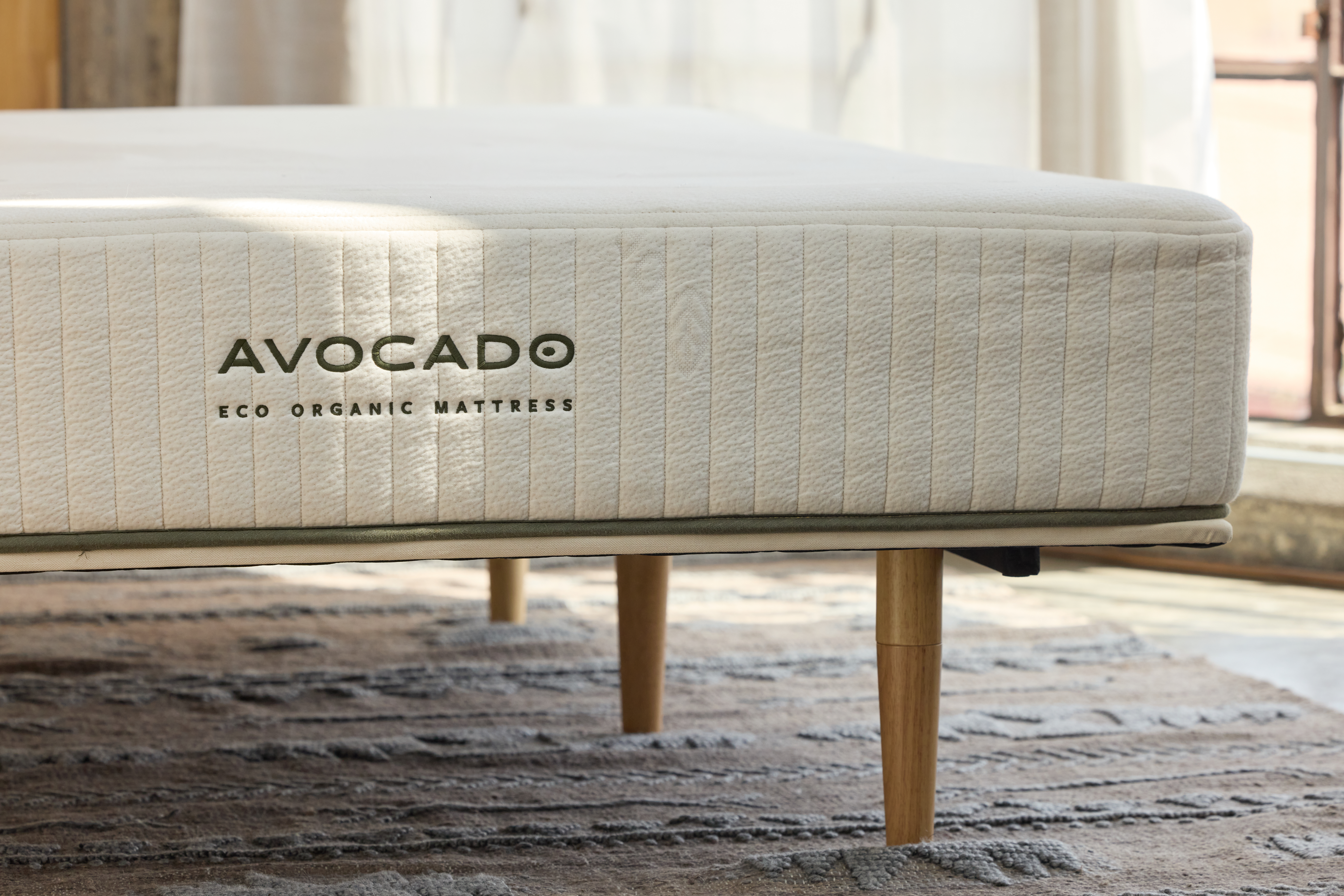 Close-up of Avocado cream-colored mattress on wood base with legs. 