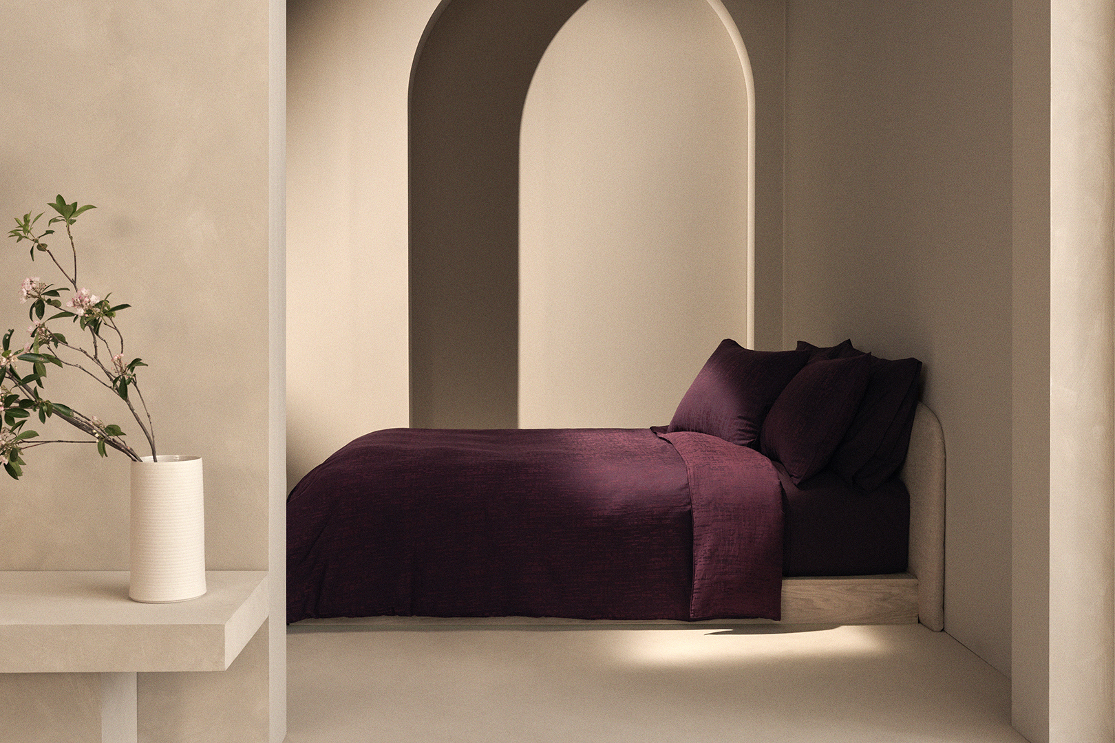 Plaster walls with arch and burgundy bed beneath.