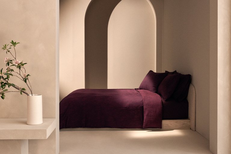 Plaster walls with arch and burgundy bed beneath.