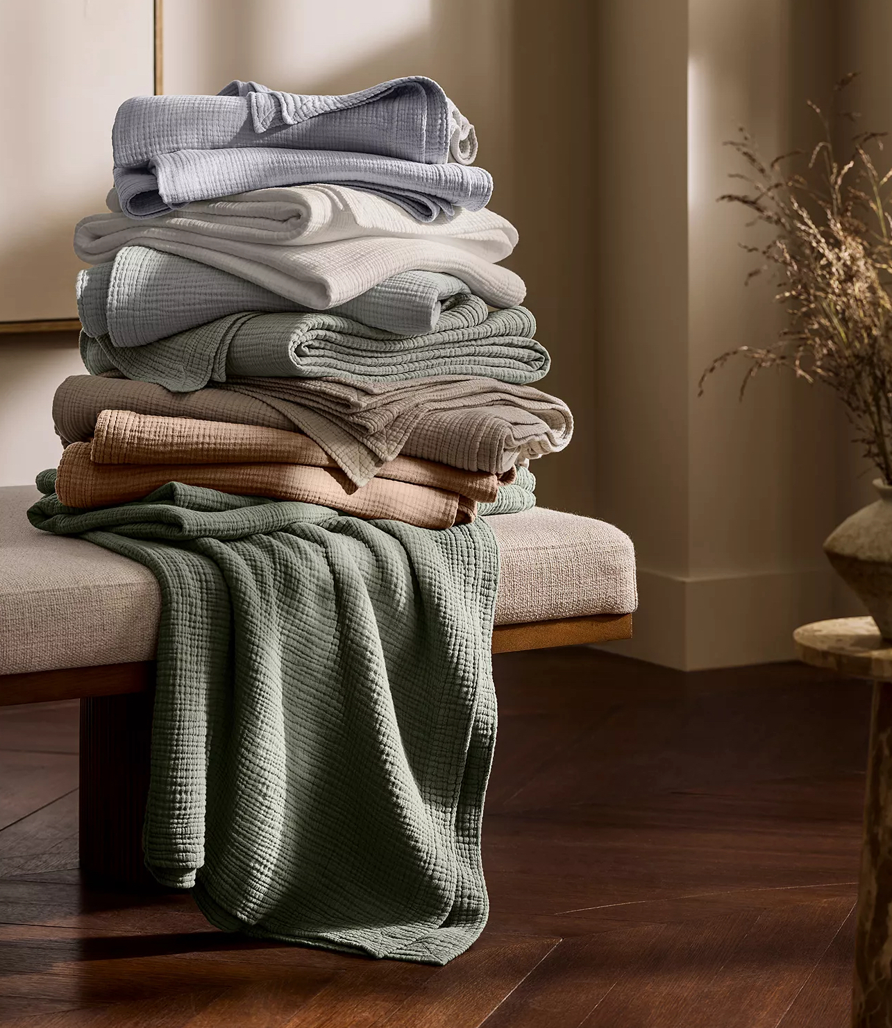 Stack of earth-toned cotton voile blankets on a bench.