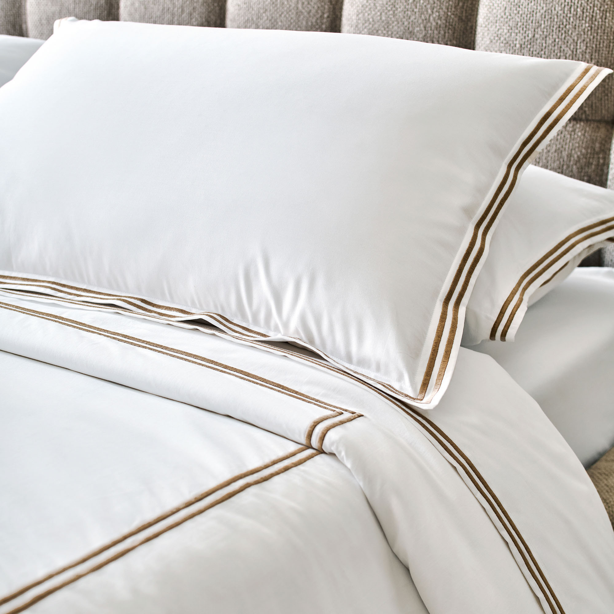 Bed close-up with white sheets with gold striped stitching.