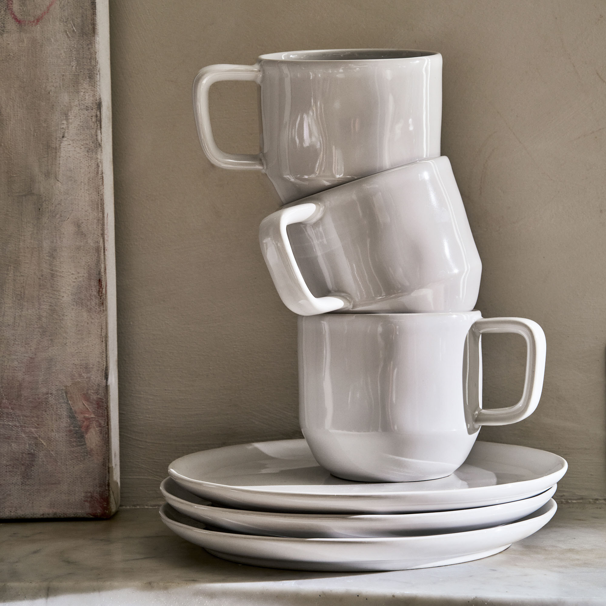 Stack of three white ceramic mugs and plates.