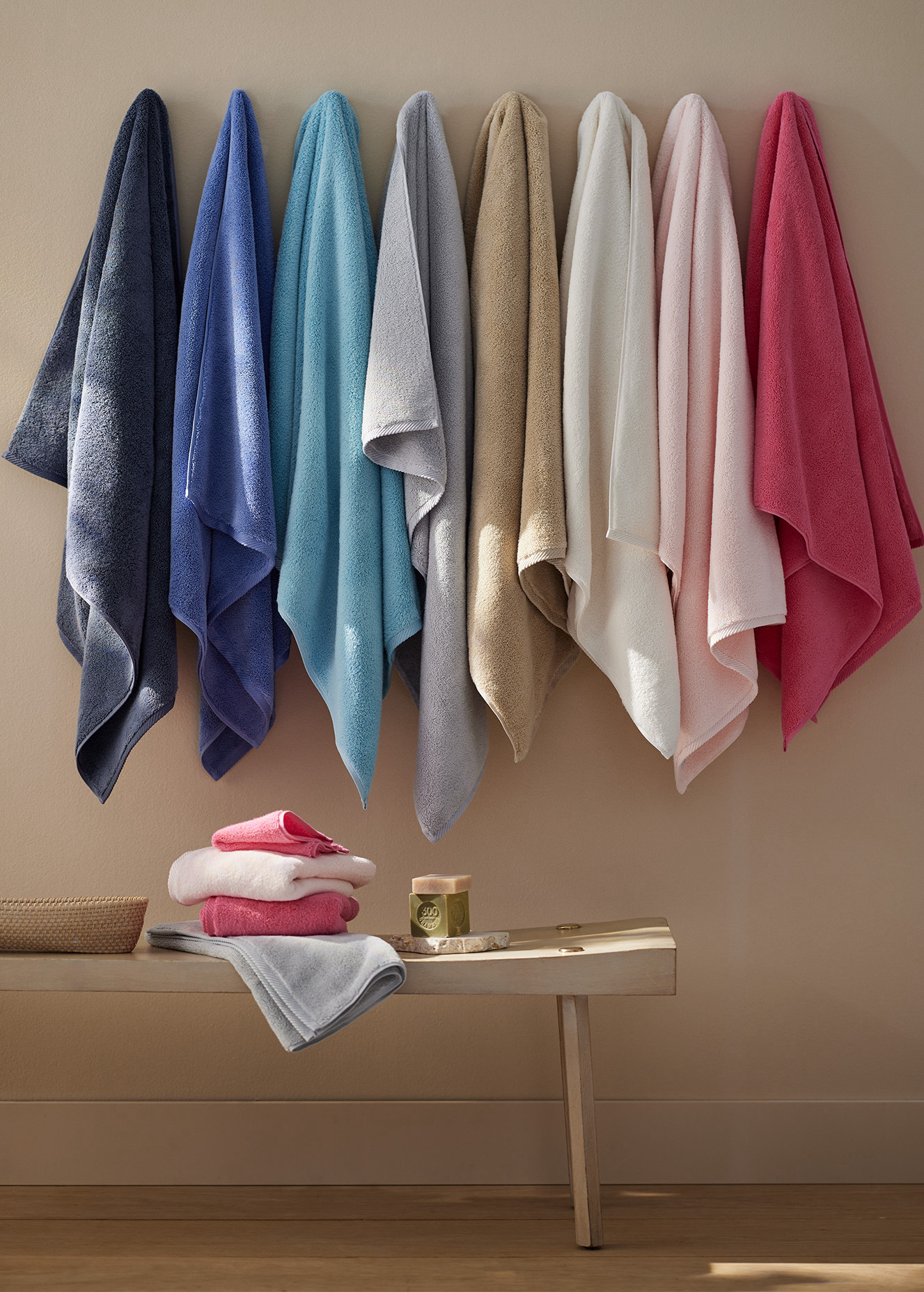 Row of hanging colorful towels against warm brown background with bench underneath.