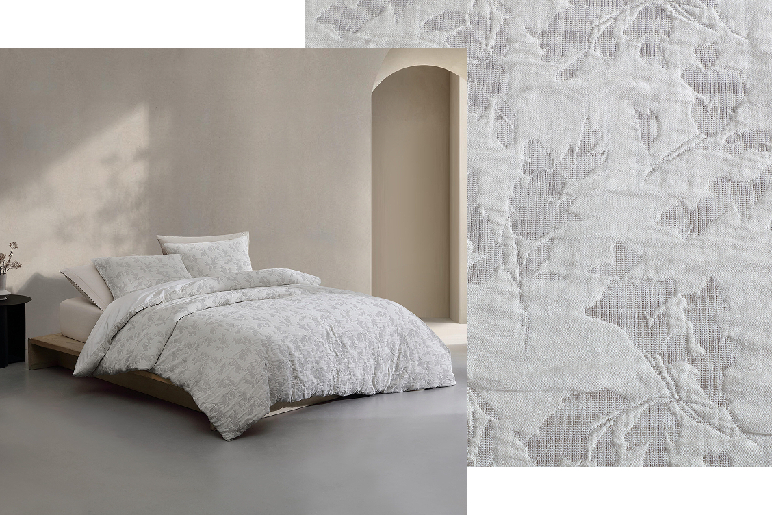 Bed near window made with white floral sheets and sheet fabric swatch layered behind image.