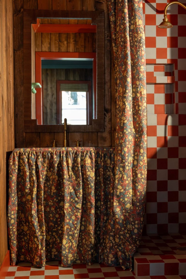 Small bathroom with red and light blue checkerboard tile and marbled fabric sink skirt and shower curtain.