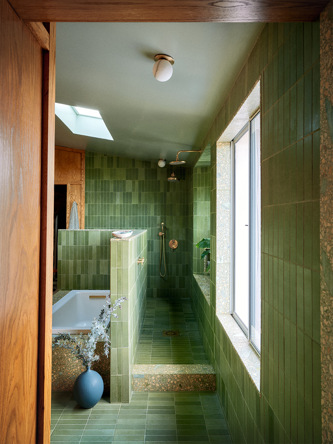 Grassy green tiled bathroom with skylight and large window on one wall.