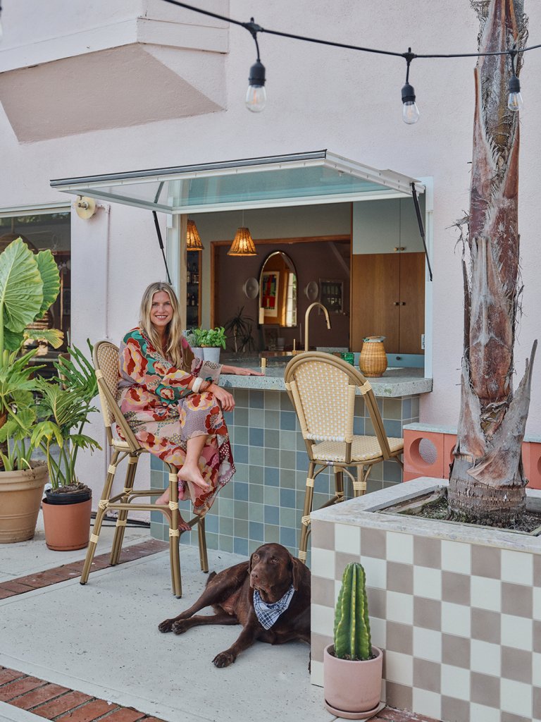 Outdoor white and turquoise tiled patio with woman seated at bar and dog laying down at her feet.