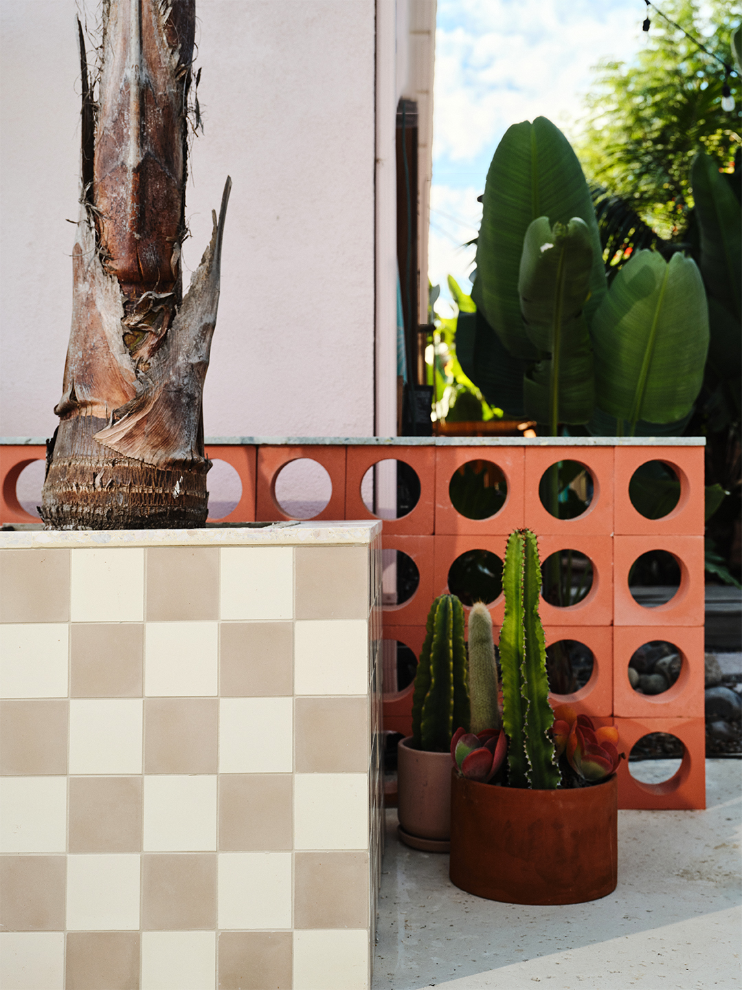 Outdoor patio with perforated red brick low divider and cream-and-beige checkerboard tile planter. 