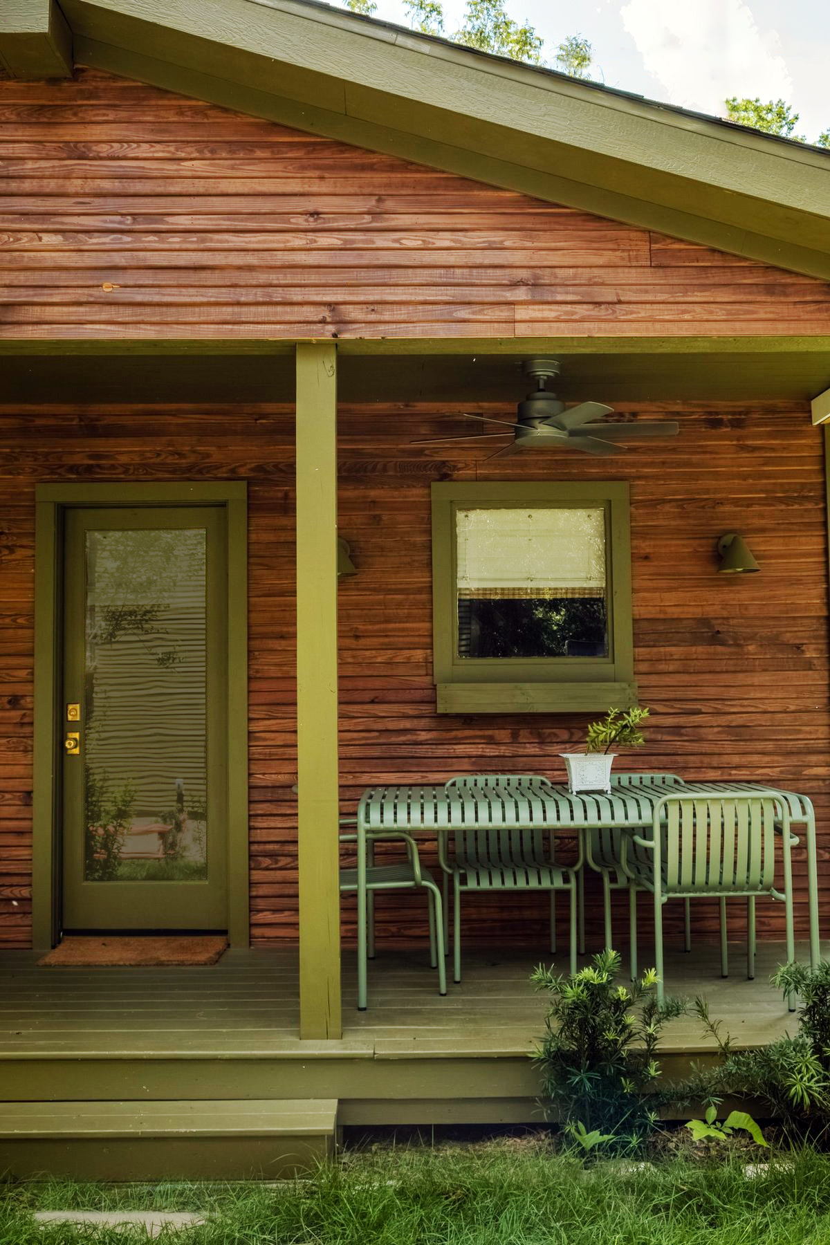 Exterior of wood bunkie house showing porch with green paint trim.