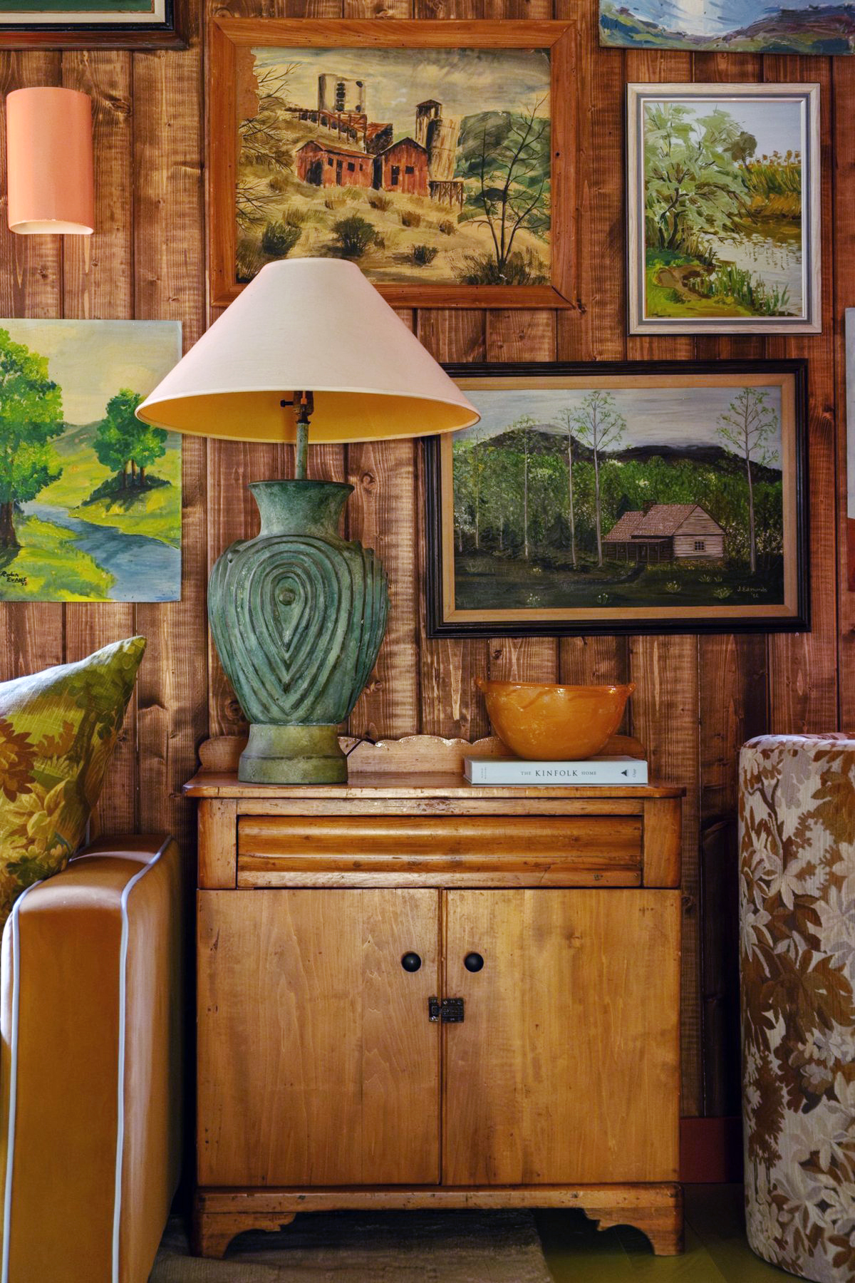 Cabin living room with vintage teal ceramic lamp and oil paintings hanging behind.
