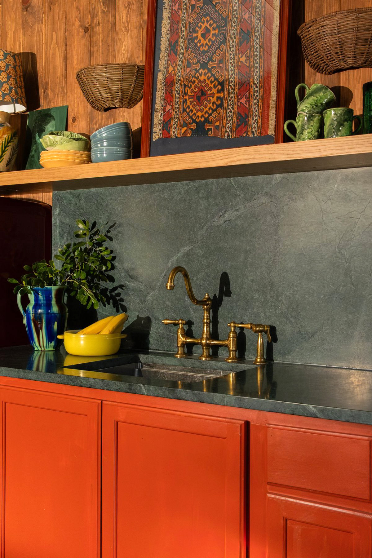 Kitchenette detail with tomato red cabinets and dark gray stone backsplash.