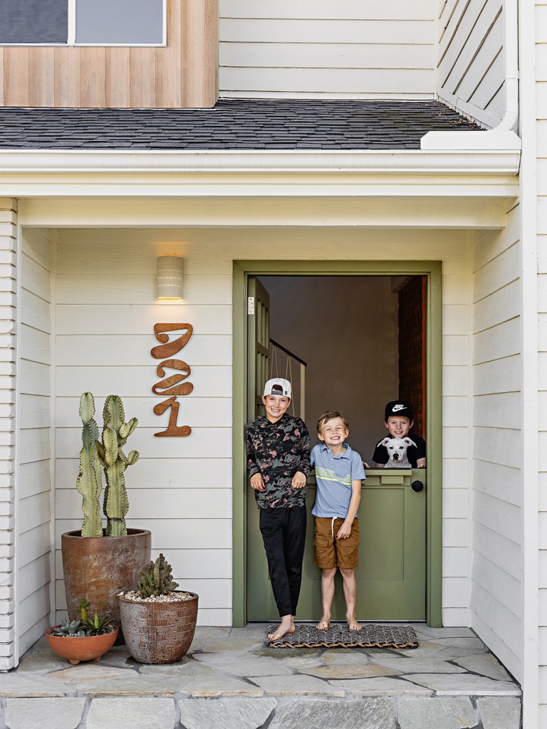 three boys and one dog at doorway of white home