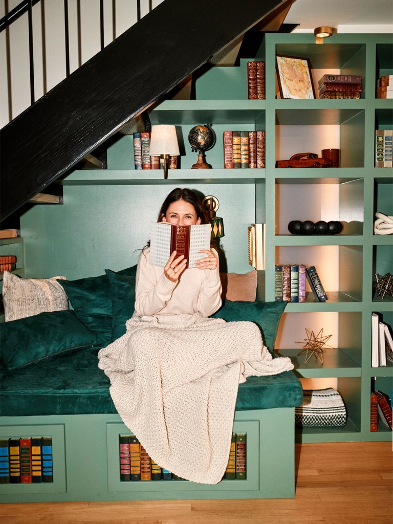 woman sitting on bench under stairs with book