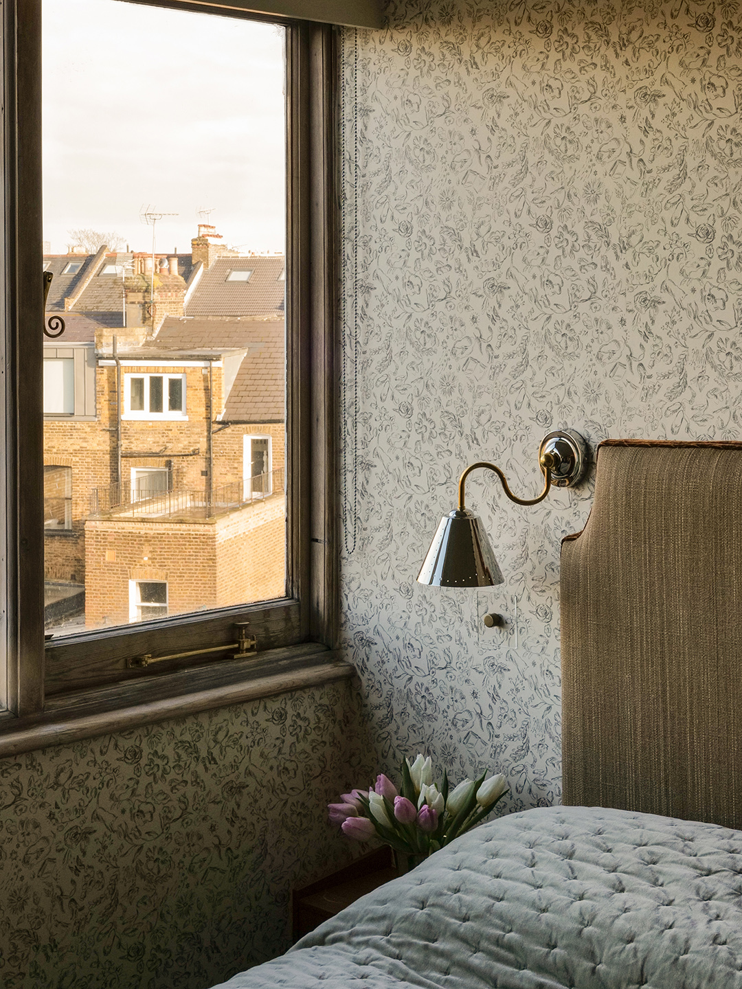 wallpapered room with bedside lamp and view out the window