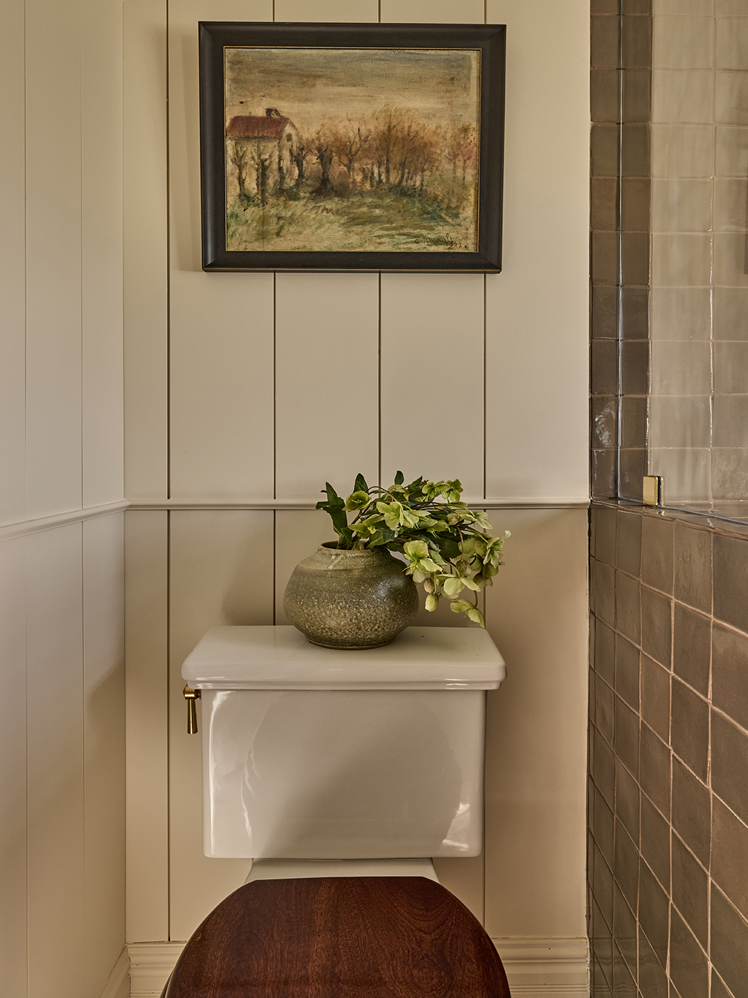 toilet with wood seat cover and artwork hanging above