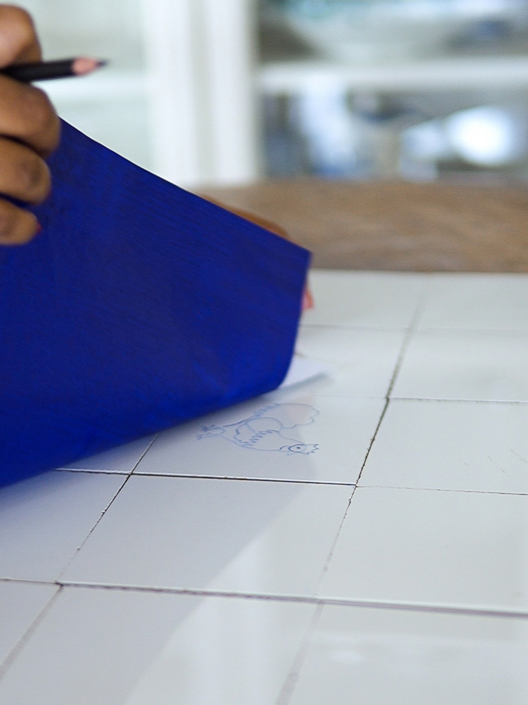 person removing tracing paper to reveal a design on tile