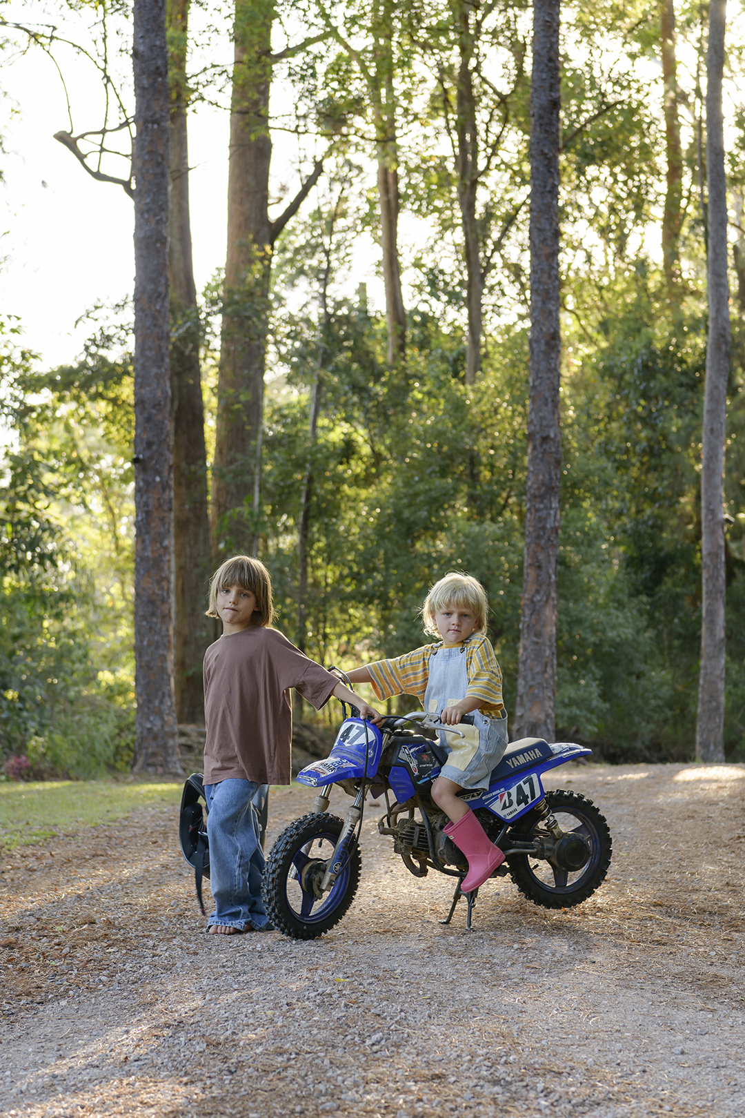 child on a dirt bike with another child in a forest
