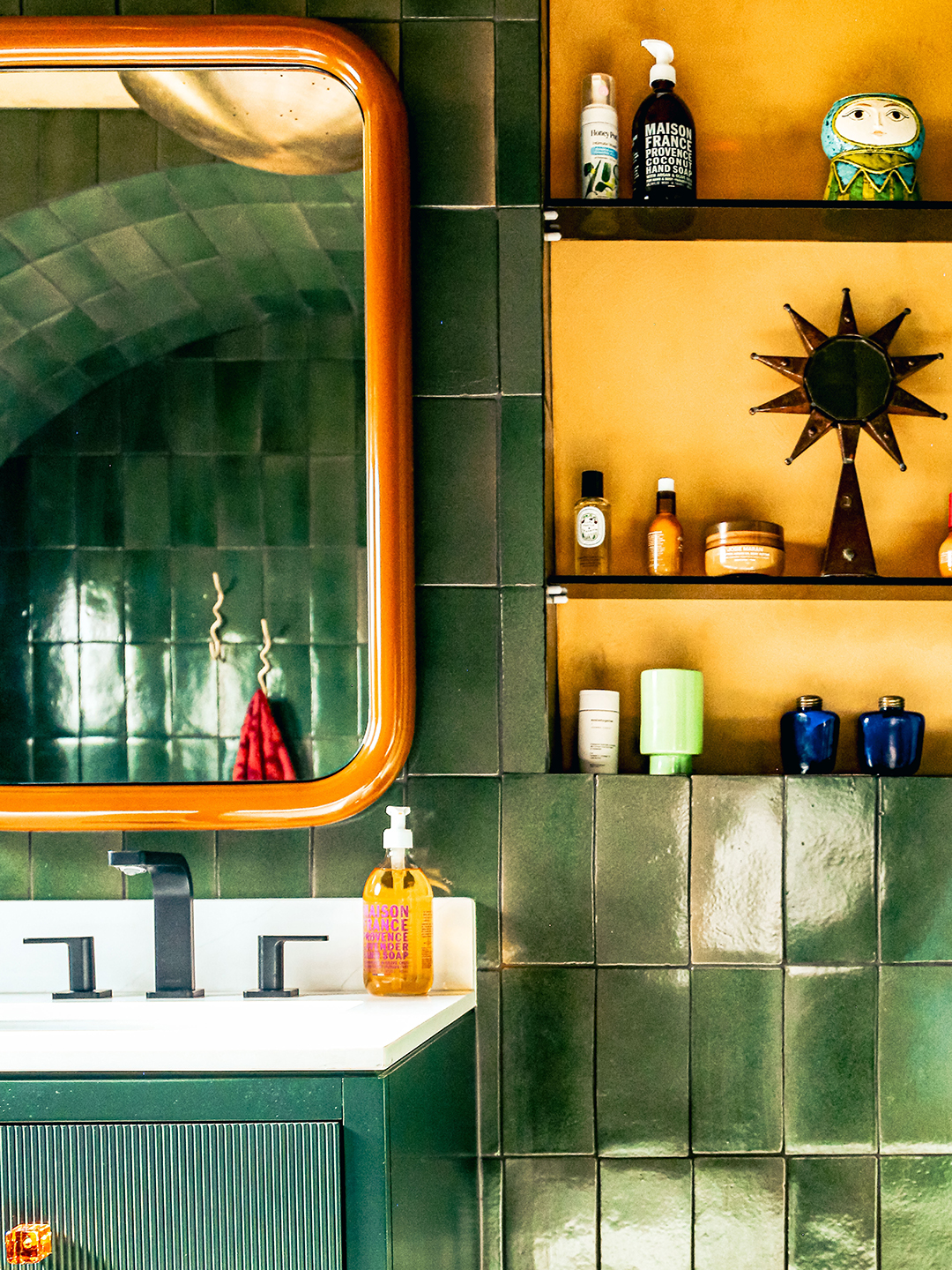 green-tiled bathroom with orange mirror and yellow shelf