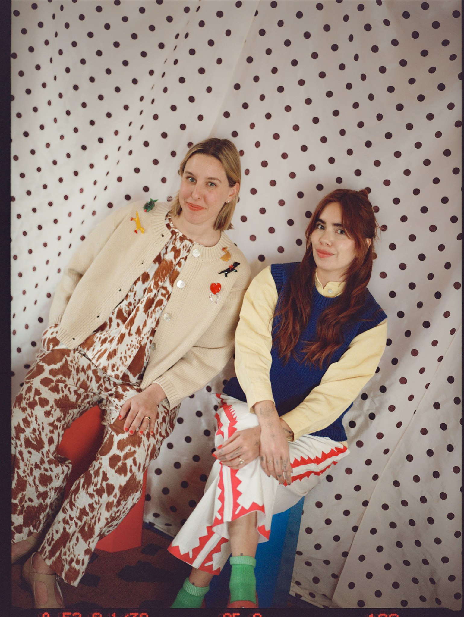 two women seated in front of a polka dot curtain