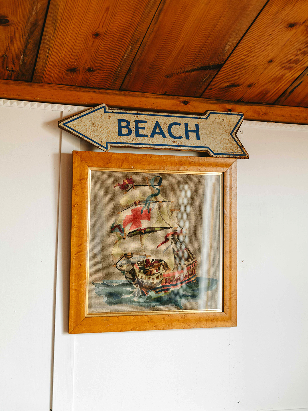 arrow-shaped beach sign above a needlepoint of a ship