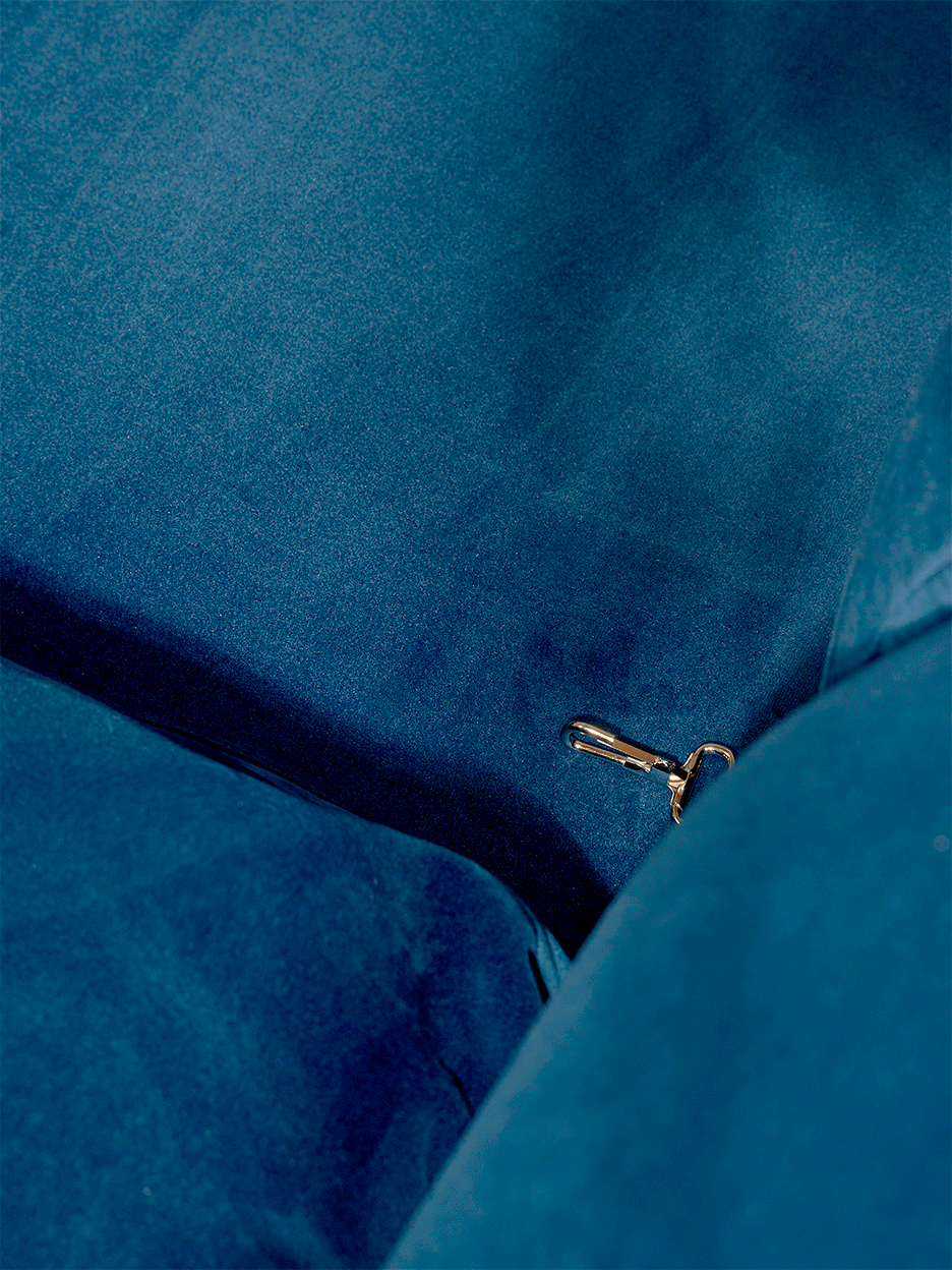 Detail of hands clipping cushion to seat on blue velvet sofa. 